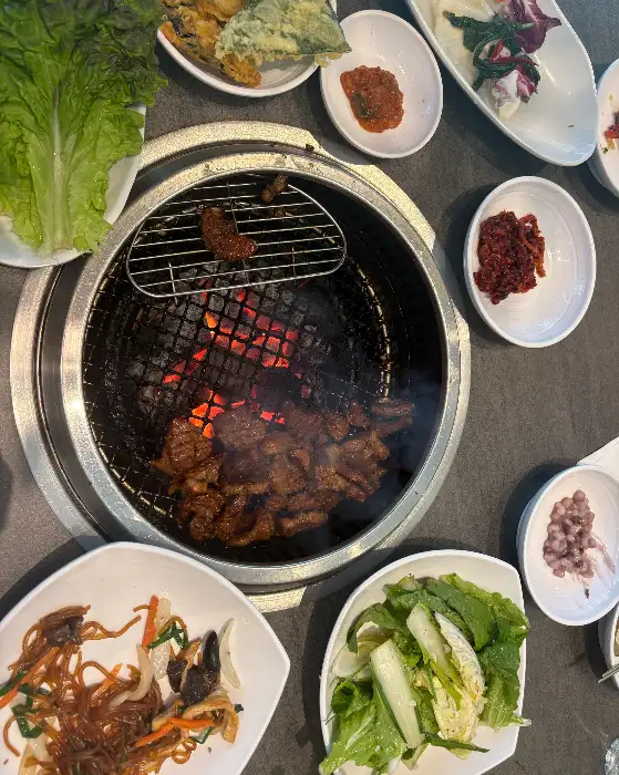 다양한 밑반찬과 숯불 위에서 구워지고 있는 고기, 그리고 신선한 쌈 채소