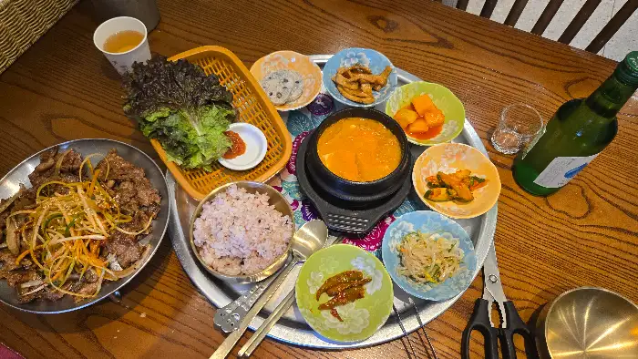 청국장, 밥, 메인 요리, 그리고 여러 가지 반찬이 한 상 가득 차려진 모습.