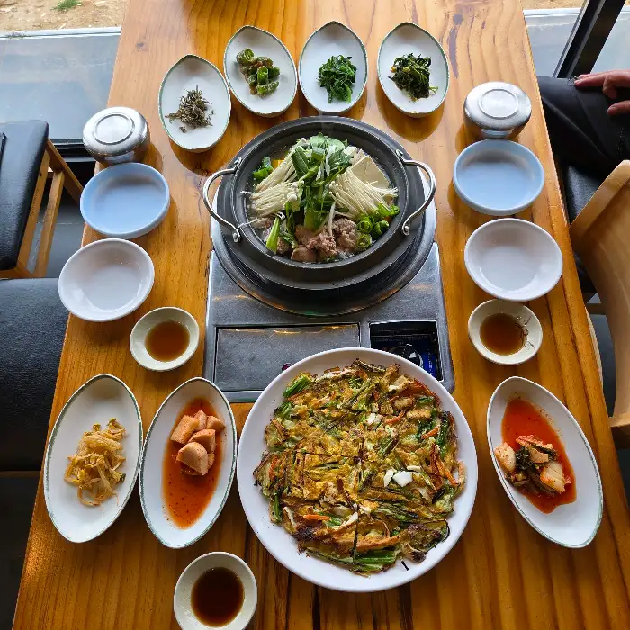 테이블 위에 놓인 젓국갈비전골, 감자전, 그리고 다양한 밑반찬들