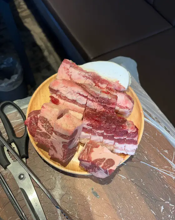 신선한 돼지고기 덩어리가 나무 접시에 담겨 있는 사진. 붉은 살코기와 하얀 비계가 조화롭습니다.