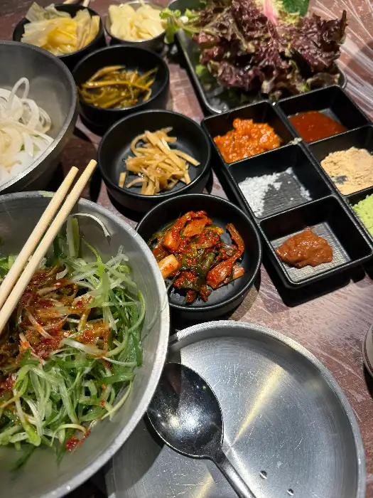 테이블에 차려진 다양한 밑반찬과 소스들. 여러 개의 작은 그릇에 다채로운 음식들이 담겨 있습니다.