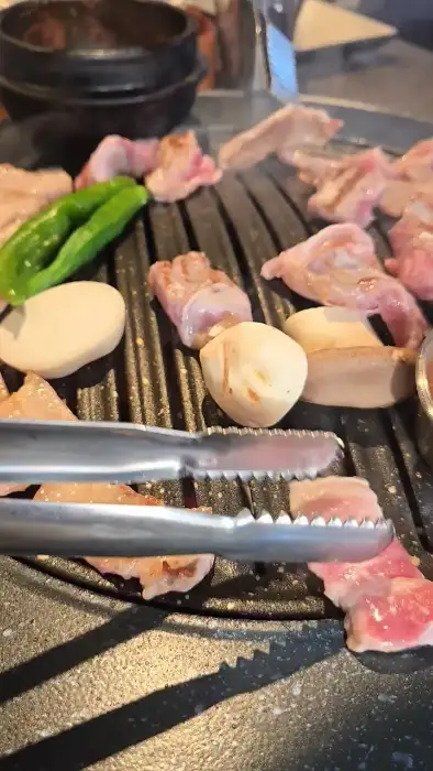 집게로 고기를 뒤집고 있는 모습. 숯불 위에 올라간 고기가 노릇하게 익어가고 있다.