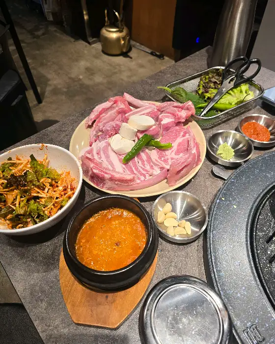 플레이팅 된 두툼한 고기와 강된장, 쌈채소, 밥 등이 함께 담겨 있는 상차림.