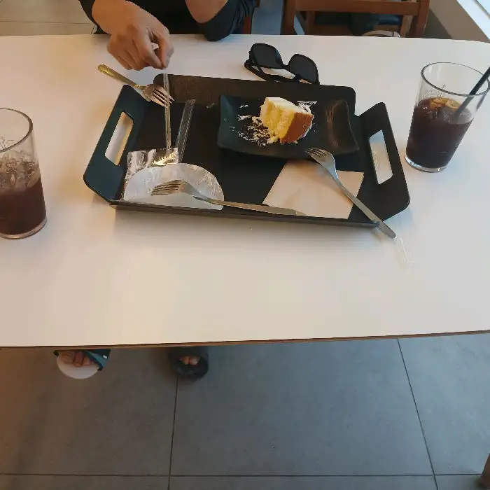 테이블 위에 놓인 케이크 조각과 아이스 아메리카노. 포크와 나이프가 준비되어 있다.