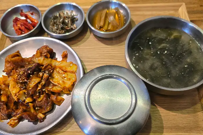 제육볶음으로 보이는 메인 요리와 함께 밥, 찌개, 그리고 몇 가지 반찬이 놓여 있는 모습.
