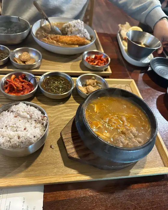 따뜻한 국물이 담긴 뚝배기 찌개와 밥, 그리고 몇 가지 반찬이 차려진 모습.