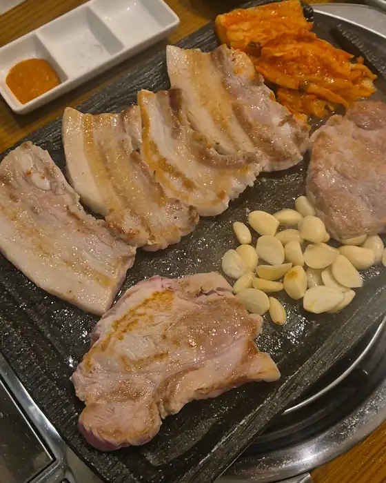 돌판에 구워지는 삼겹살, 김치, 마늘의 모습
