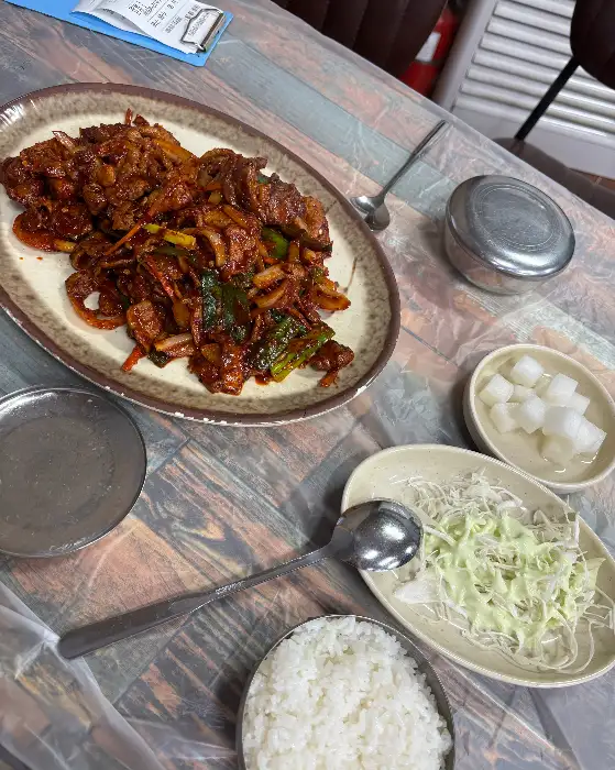 식탁 위에 차려진 제육볶음, 밥, 샐러드, 깍두기 등의 모습