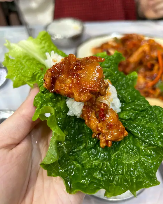 상추 위에 밥과 제육을 올려 쌈을 싸고 있는 모습