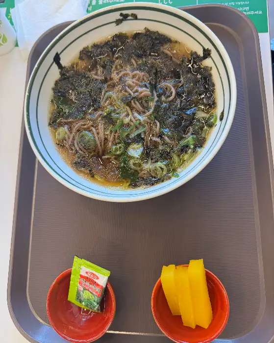 냉모밀 한 그릇. 짙은 국물 위에 김가루와 파가 뿌려져 있고, 면발이 보인다.
