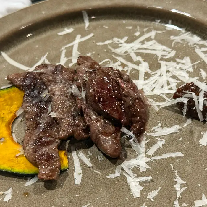 흰 가루가 뿌려진 접시에 여러 조각의 잘 익은 소고기와 얇게 썬 호박, 그리고 으깬 감자가 놓여 있습니다.