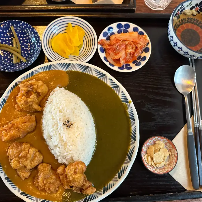 카레 위에 큼직한 가라아게와 새우, 돈까스 조각이 토핑으로 올라간 모습. 곁들임 반찬도 보인다.