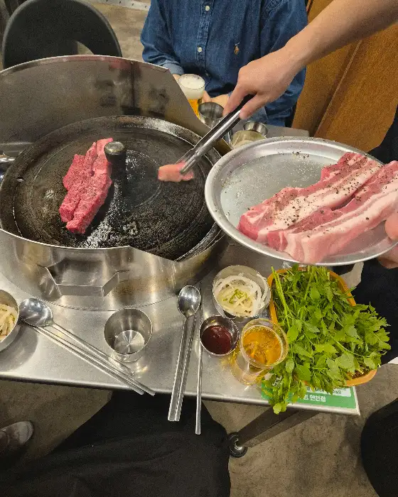 직원이 솥뚜껑 위에서 삼겹살을 굽고 있는 모습