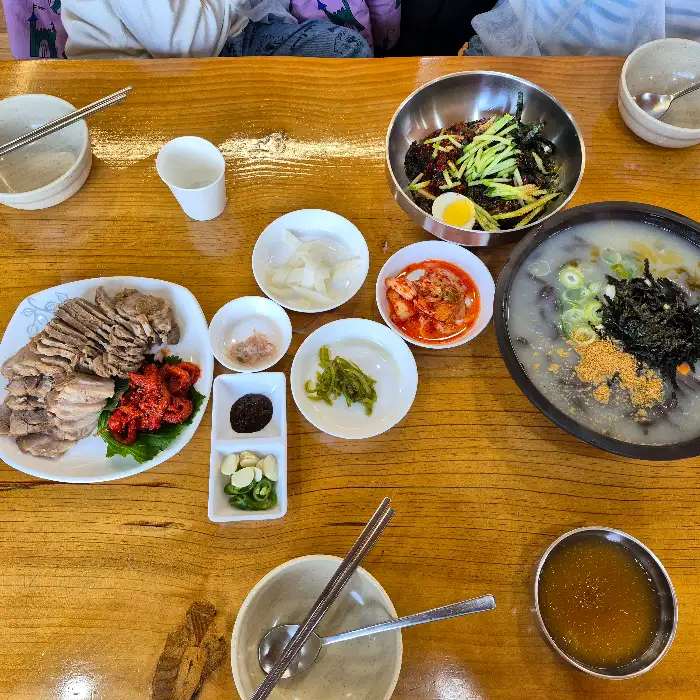 식탁 위에 여러 가지 음식들이 차려져 있습니다. 수육, 막국수, 옹심이, 김치 등이 보입니다.