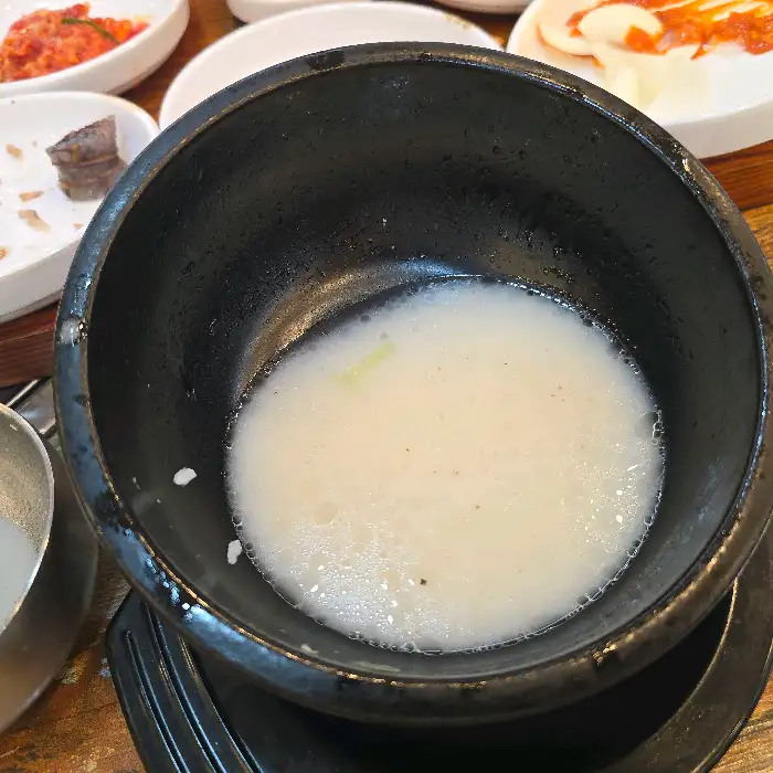 뚝배기에 담겨 나온 국밥의 근접샷, 뽀얀 국물 위로 파와 들깨가루가 뿌려져 있습니다.