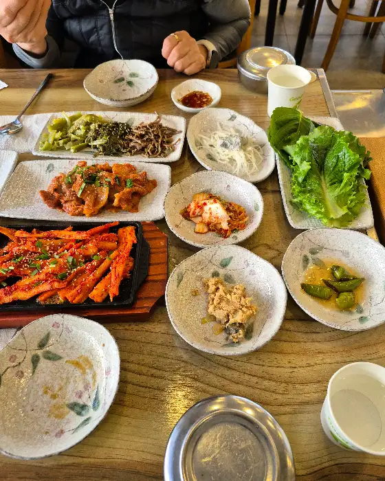 다양한 나물 반찬과 제육볶음, 더덕구이가 차려진 테이블 세팅