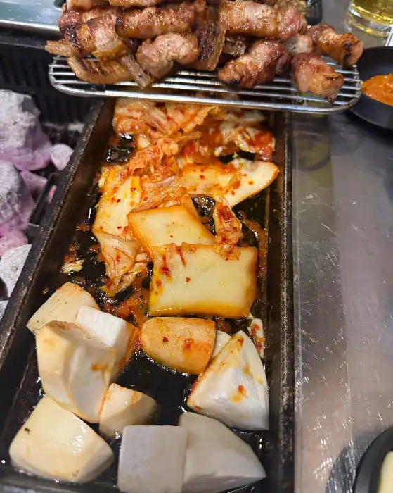 불판 위에서 익어가고 있는 두툼한 삼겹살과 곁들임 채소들