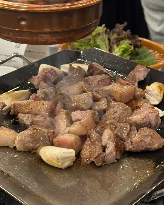 불판 위에서 맛있게 익어가고 있는 고기와 마늘, 양파 등의 모습