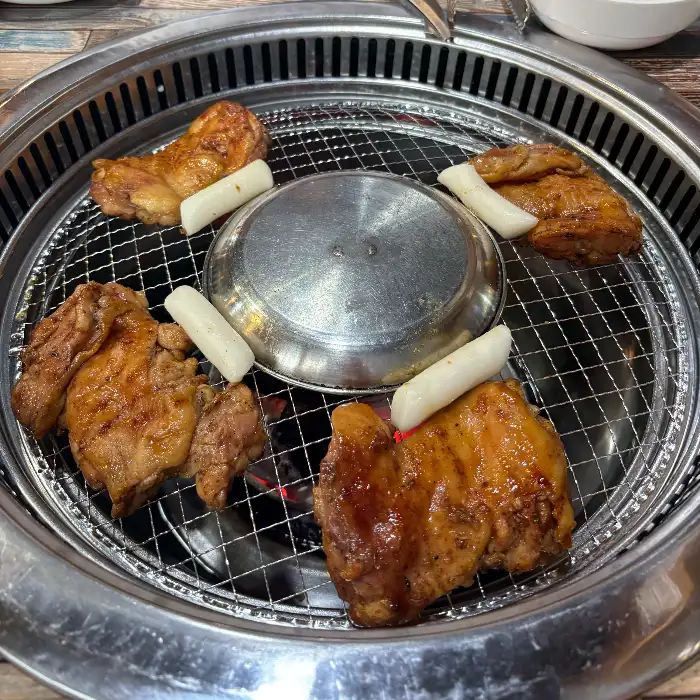 숯불 위에서 익어가는 닭갈비 조각과 떡