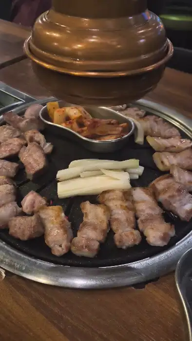 불판 위에서 익어가는 고기와 파김치, 마늘 등.