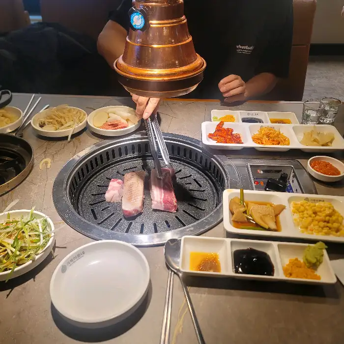 불판 위에서 구워지고 있는 삼겹살과 곁들임 찬들
