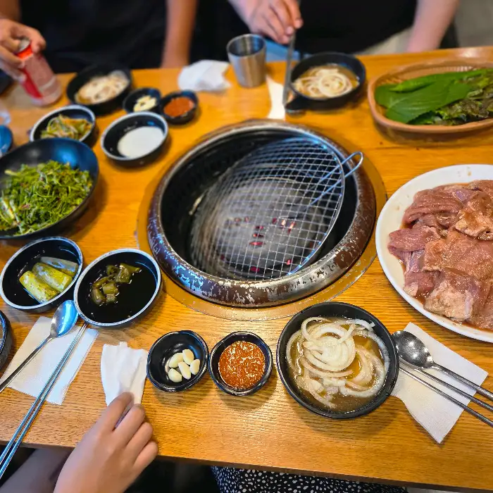 테이블에 차려진 갈비와 다양한 밑반찬, 그리고 숯불 그릴