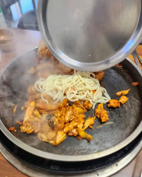 철판 위에서 익고 있는 닭갈비와 우동사리