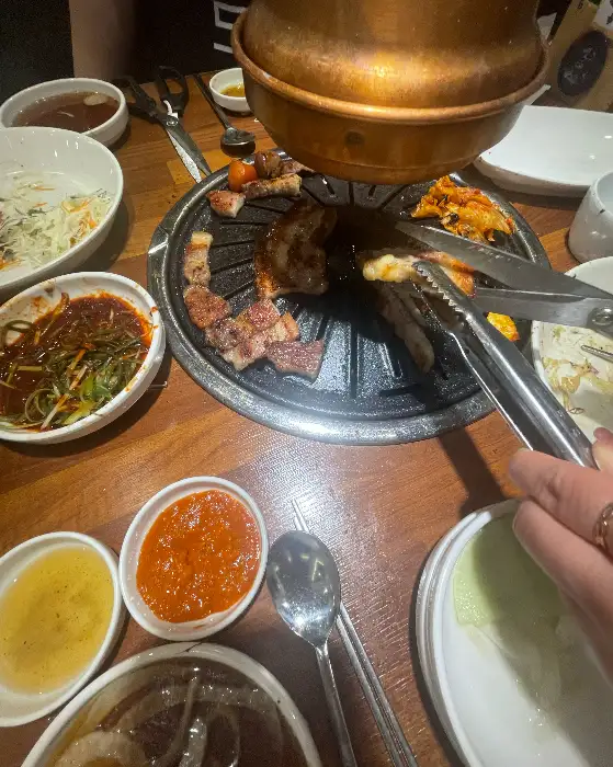 불판 위에서 익어가는 삼겹살과 떡볶이, 샐러드 등의 모습