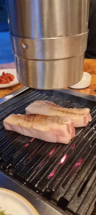 숯불 위에서 두툼한 흑돼지 조각들이 천천히 익어가고 있는 모습