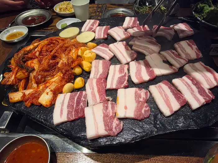돌판 위에 삼겹살, 김치, 감자가 함께 구워지고 있는 모습