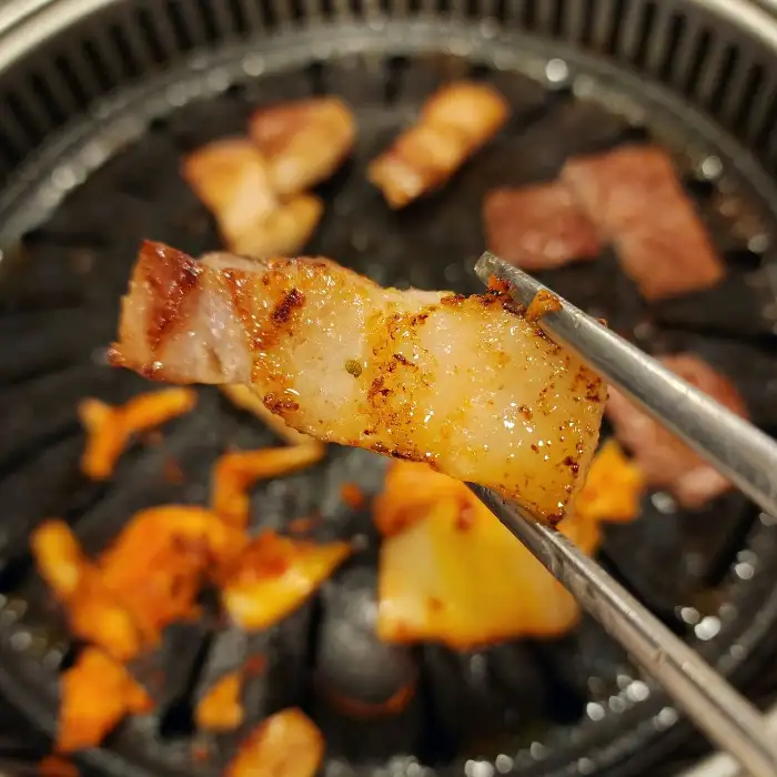 집게로 잡은 큼직한 삼겹살 조각이 맛있게 익어가고 있다.