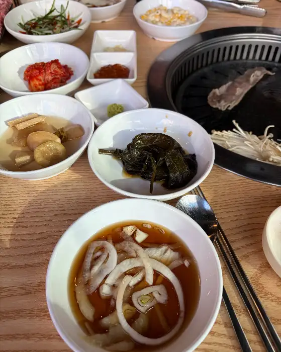 테이블 위에 차려진 다양한 반찬들, 가운데는 쌈장이 담긴 작은 종지.