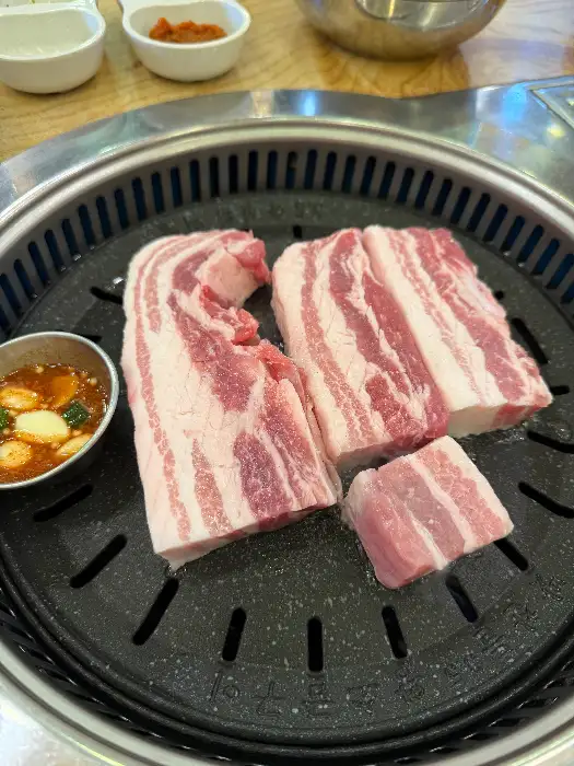 불판 위에 올려진 먹음직스러운 삼겹살 덩어리