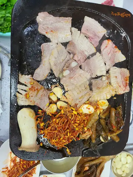 뜨겁게 달궈진 돌판 위에서 구워지는 삼겹살과 곁들임 재료들
