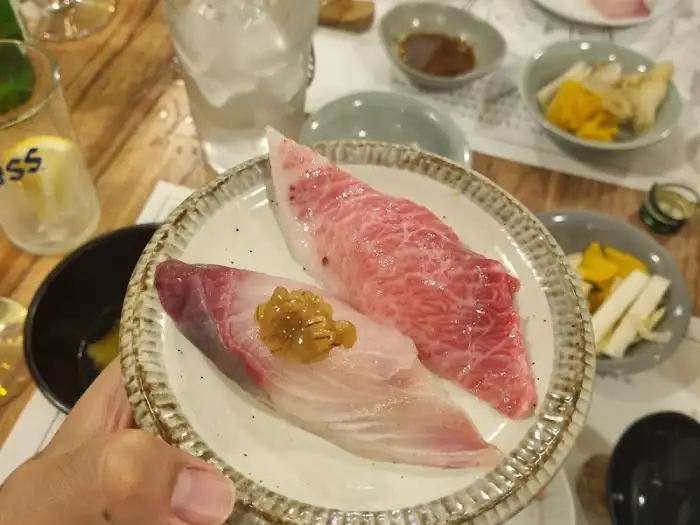 손에 들고 있는 접시에 신선한 생선회 두 점이 담겨 있고, 와사비가 올려져 있음