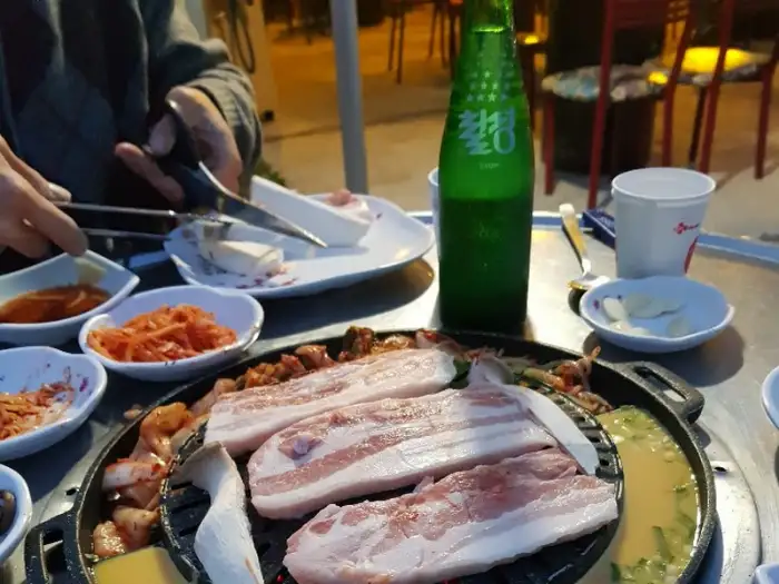 삼겹살과 함께 놓인 술병과 밑반찬