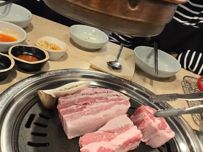 넓은 불판 위에 여러 덩어리의 삼겹살과 버섯이 올라가 있습니다.