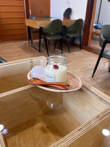 막걸리 푸딩. 투명한 유리병에 담긴 하얀 푸딩 위에 장미꽃 한 송이가 올려져 있습니다.