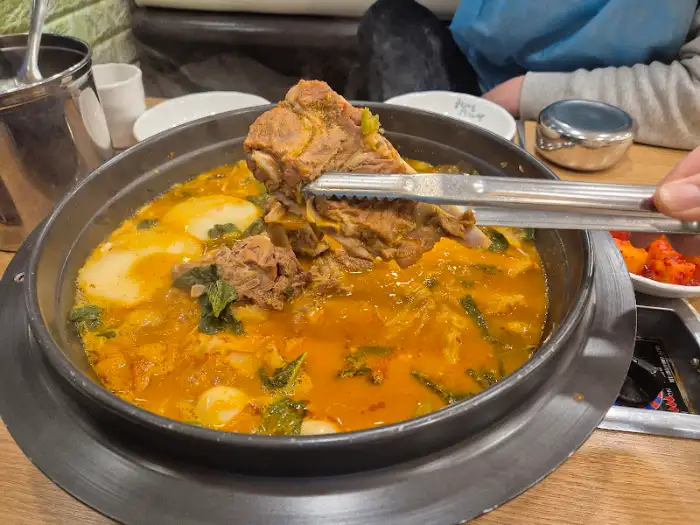 묵은지 감자탕 뚝배기에서 뼈를 건져 올리는 모습