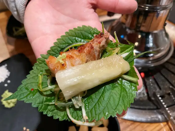 잘 구워진 오겹살 한 점을 깻잎에 싸서 먹는 모습