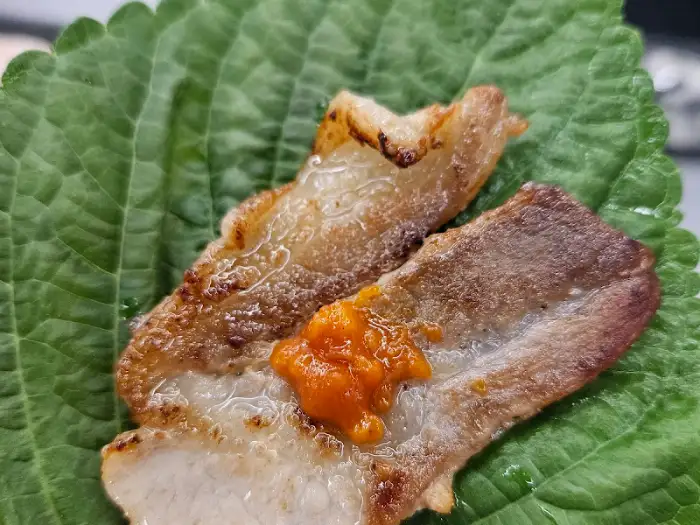 깻잎 위에 올려진 구워진 삼겹살 조각과 양념