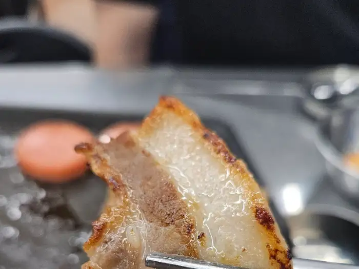 집게로 집어 올린 잘 구워진 삼겹살 조각