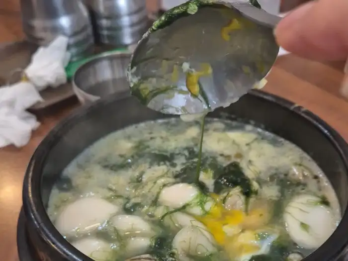 매생이굴떡국의 한 스푼, 굴과 떡, 매생이가 조화롭게 담겨 있음