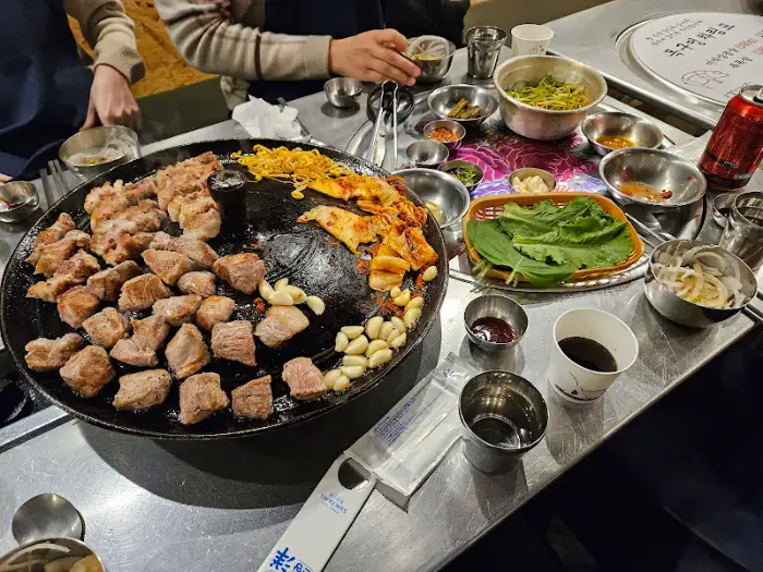 솥뚜껑에 삼겹살, 갓김치, 콩나물이 구워지는 모습