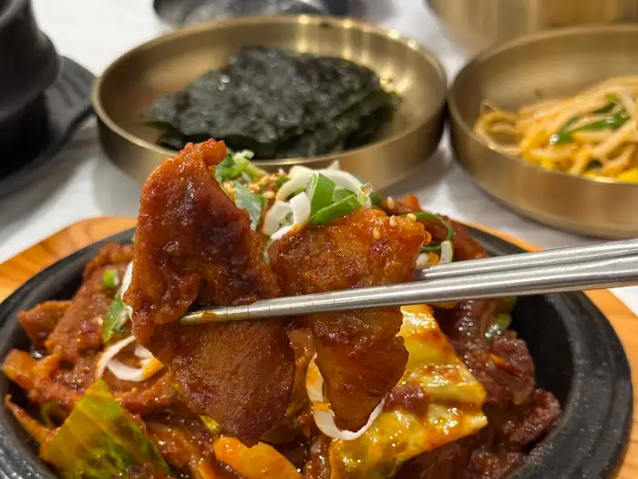 철판 삼겹 쭈꾸미를 집게로 집어 올리는 모습