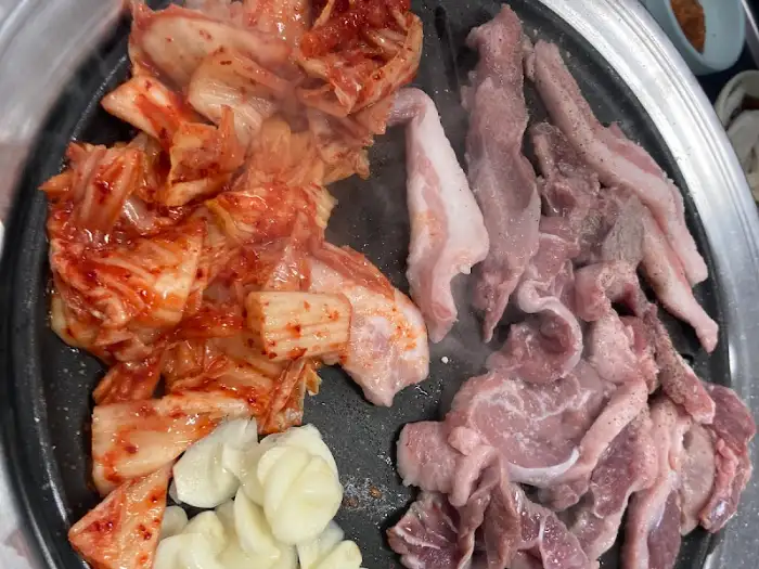 불판 위에서 익어가는 뒷고기와 김치, 마늘
