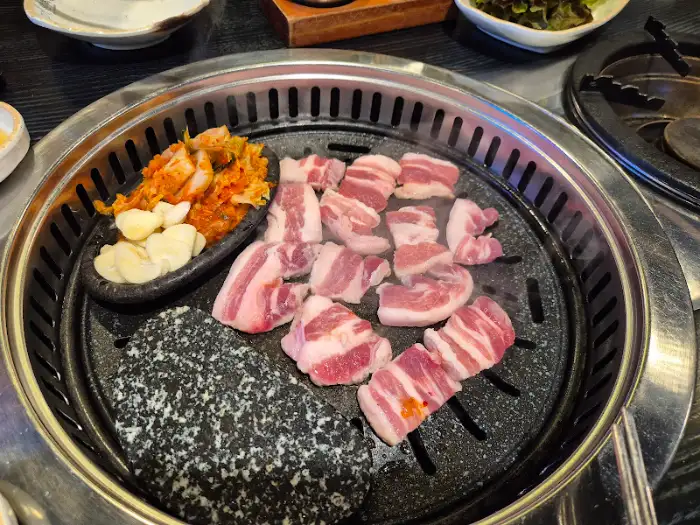 솥뚜껑 위에서 구워지는 삼겹살과 김치, 마늘