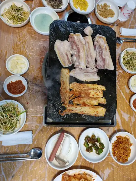 테이블 위에 놓인 솥뚜껑과 삼겹살, 반찬들