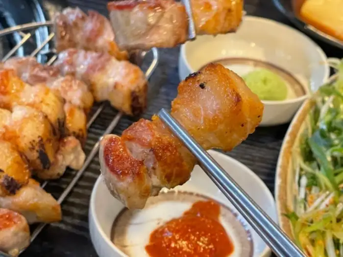 집게로 집어 올린 잘 구워진 삼겹살 조각