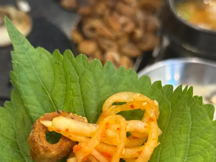 두 개의 집게가 진한 국물이 담긴 뚝배기 속 막창 조각 하나를 들어 올리고 있다. 뚝배기 안에는 대파와 양파 등 채소도 함께 들어 있다.